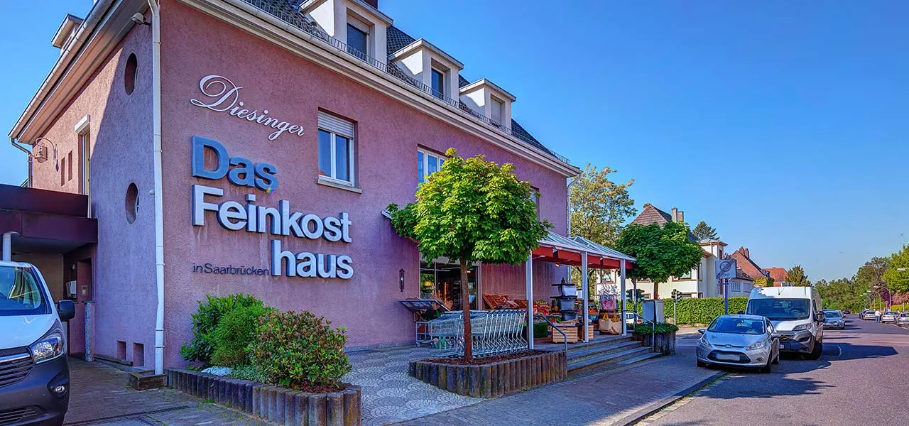 Das Feinkosthaus von außen: rosafarbenes Eckhaus mit Schriftzug und Vordach